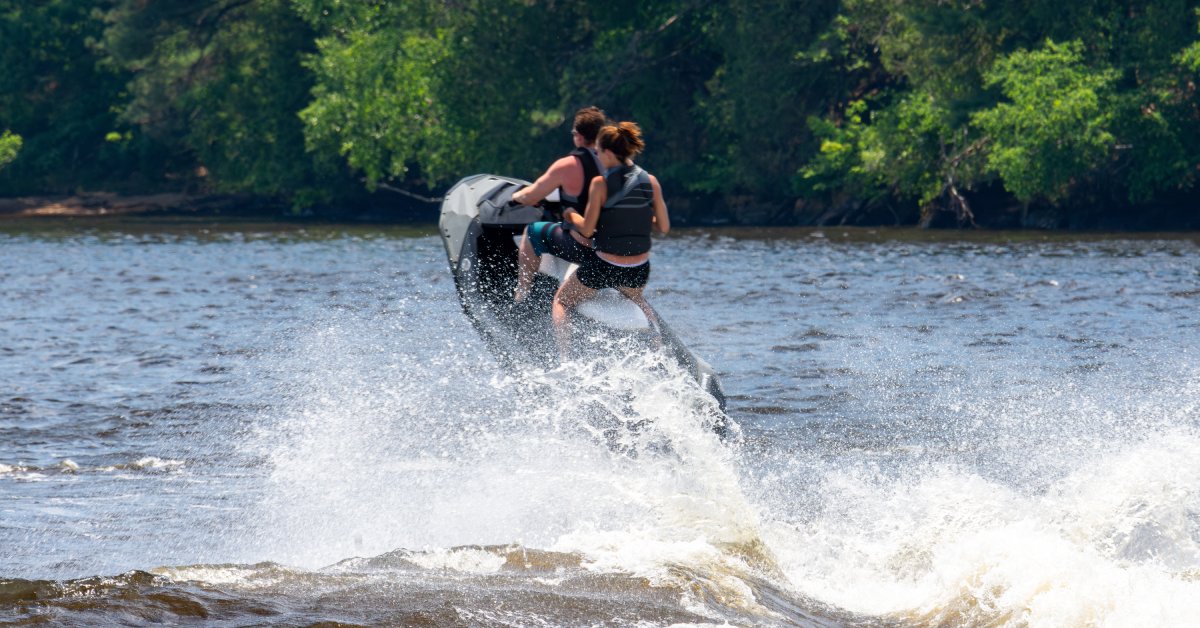 Understanding Jet Ski Horsepower Ratings A man and a woman riding on a jet ski on a sunny day. The jet ski is airborne and making waves around them.