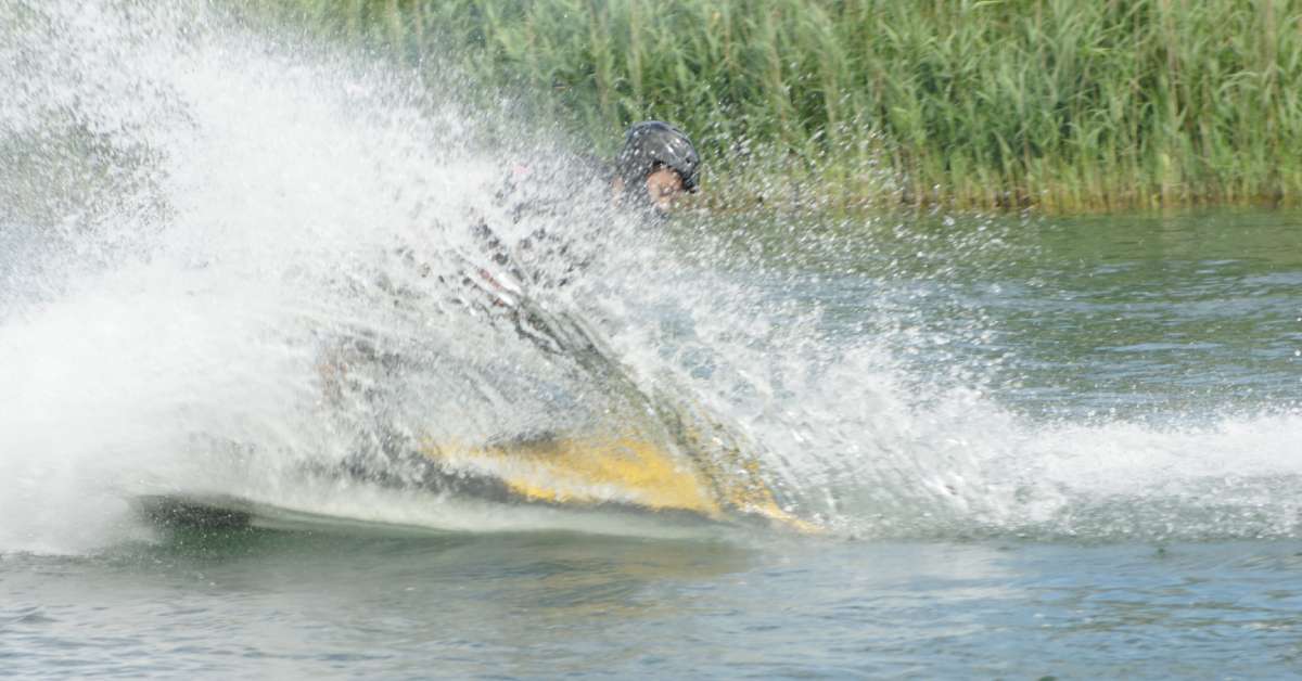 A person riding a jet ski on a body of water turns sharply, blocking the view of themselves with a wave of water.