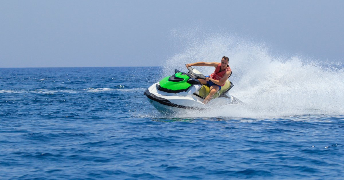 A person riding a green and white jet ski makes a sharp turn on the water, spraying a big wave in their wake.