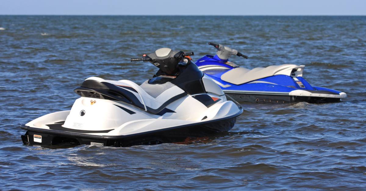 On the water, two jet skis float next to each other without drivers. One jet ski is black and the other is blue. On the water, two jet skis float next to each other without drivers. One jet ski is black and the other is blue.