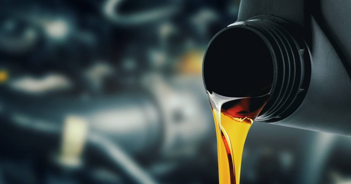 A close up look at oil coming out of a dark bottle. the oil is translucent with engine components in the background.